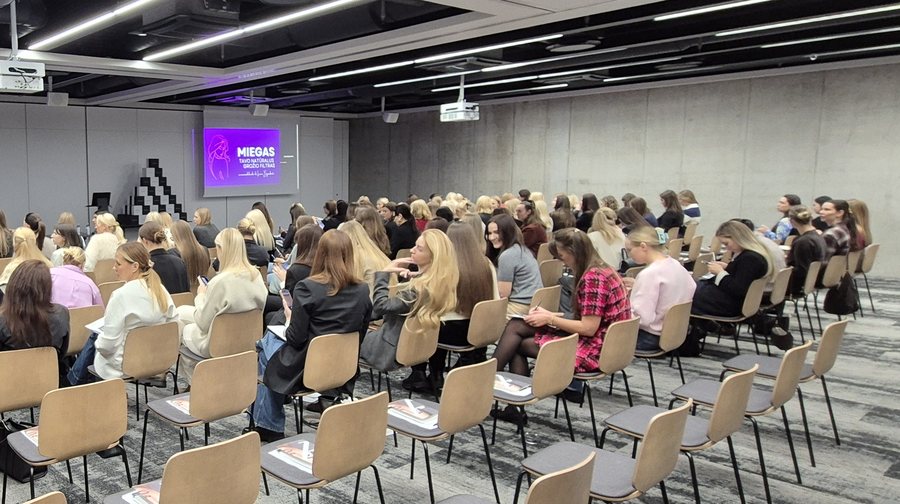 Konferencijos salė su dalyviais: projekcinis ekranas, garso sistema ir techninė įranga renginio metu.